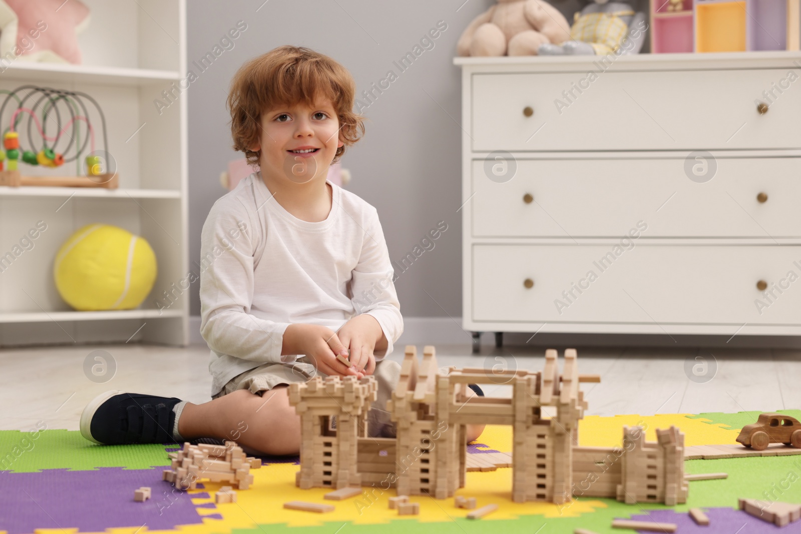 Photo of Little boy playing with wooden construction set on puzzle mat in room. Child's toy