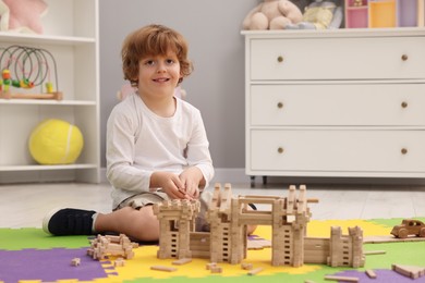 Photo of Little boy playing with wooden construction set on puzzle mat in room. Child's toy