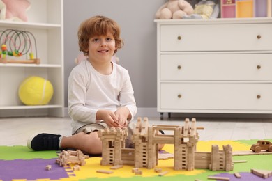 Little boy playing with wooden construction set on puzzle mat in room. Child's toy