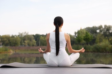 Photo of Woman practicing Padmasana on yoga mat outdoors, back view. Lotus pose