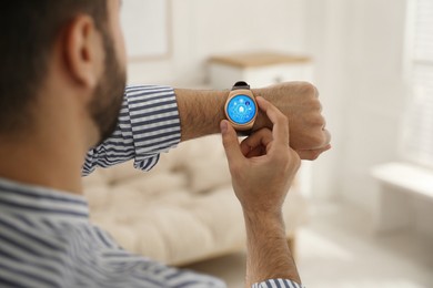 Man setting smart home control system via smartwatch indoors, closeup. App interface with icons on display