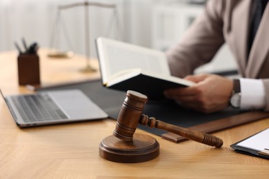 Photo of Lawyer reading book at table in office, focus on gavel