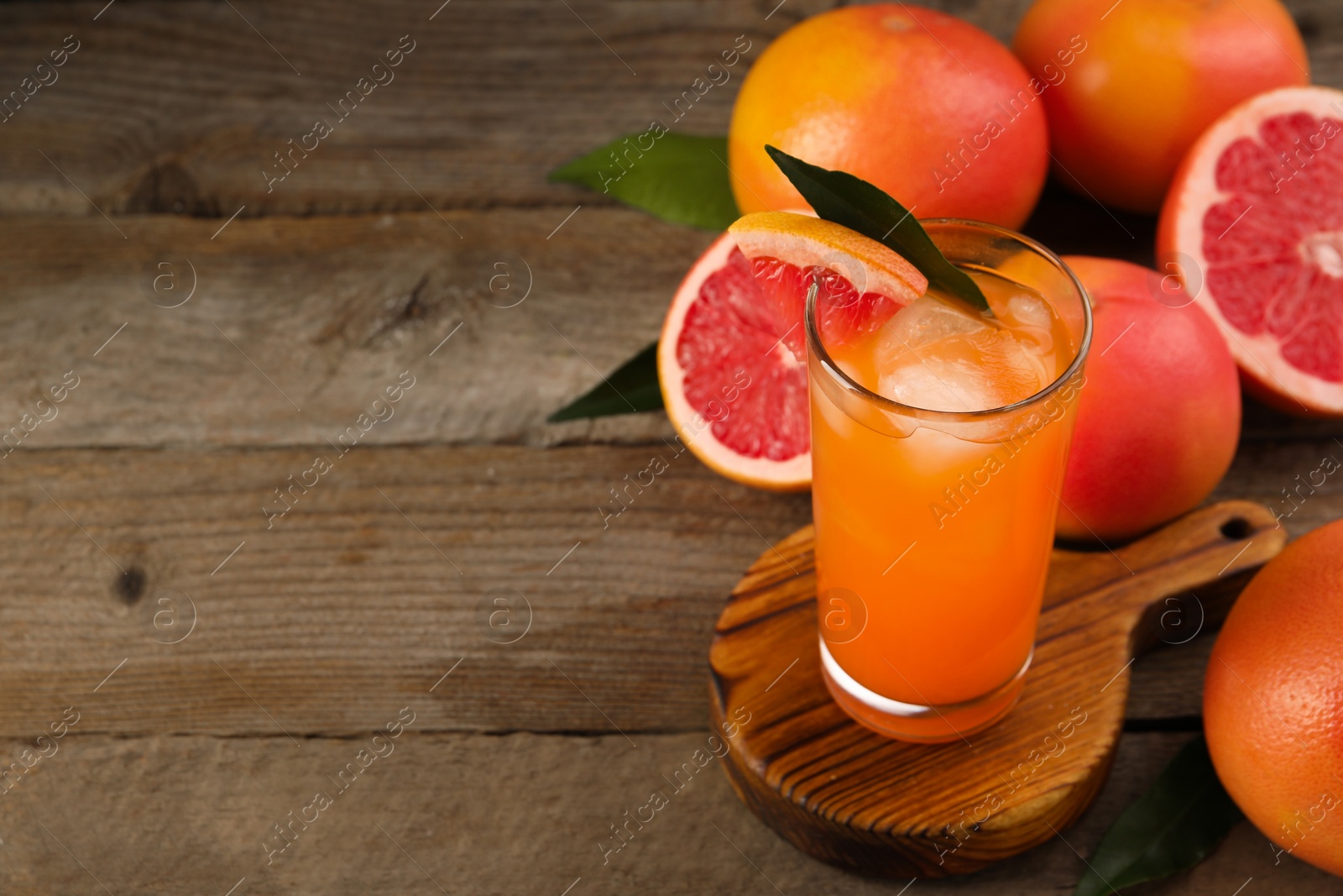 Photo of Tasty grapefruit drink with ice in glass and fresh fruits on wooden table. Space for text