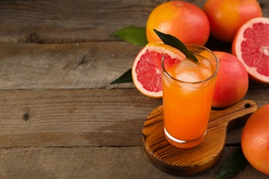 Photo of Tasty grapefruit drink with ice in glass and fresh fruits on wooden table. Space for text