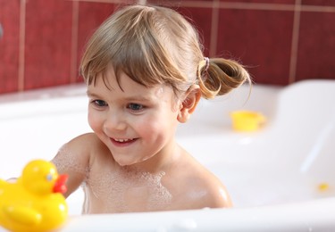 Smiling girl bathing with toy duck in tub at home, selective focus
