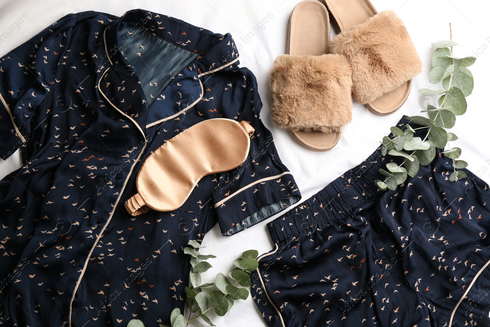 Photo of Flat lay composition with fluffy slippers and pajamas on white bedsheet. Comfortable home outfit