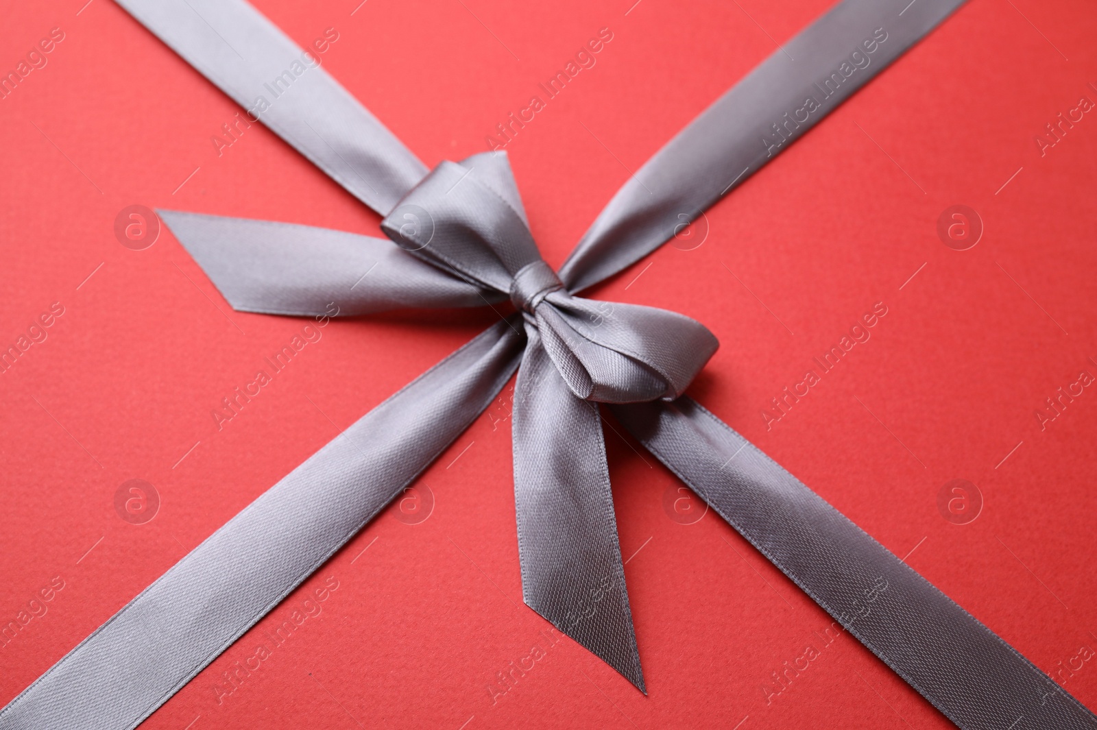 Photo of Grey satin ribbon with bow on red background