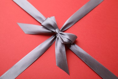 Photo of Grey satin ribbon with bow on red background