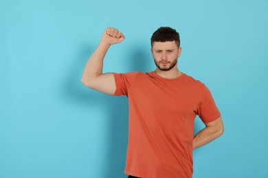 Young man showing arm on light blue background