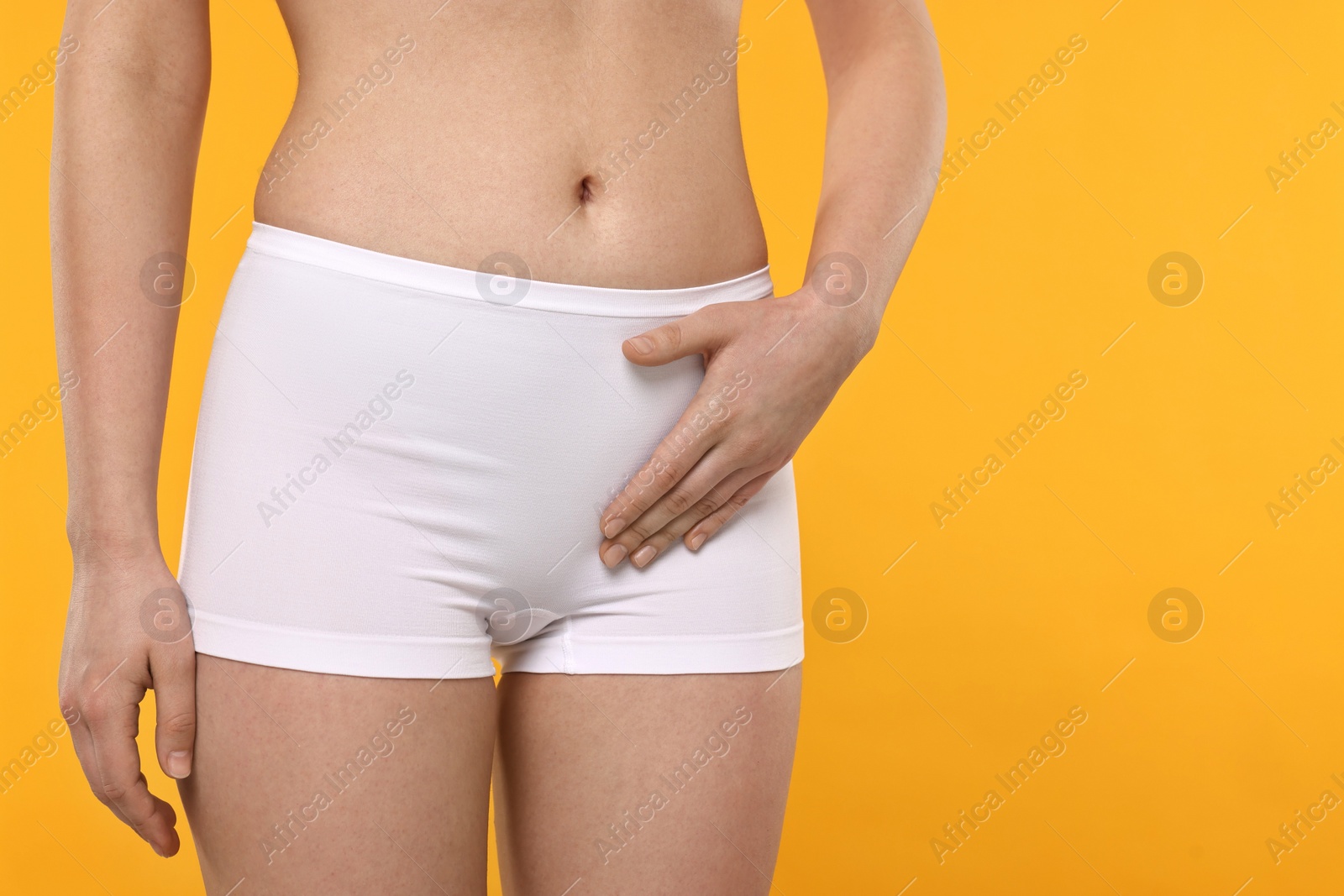 Photo of Woman holding hand near panties on orange background, space for text. Women's health
