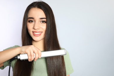 Photo of Happy woman using hair iron on grey background. Space for text