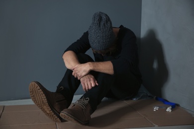 Photo of Stoned drug addict sitting on floor near grey wall