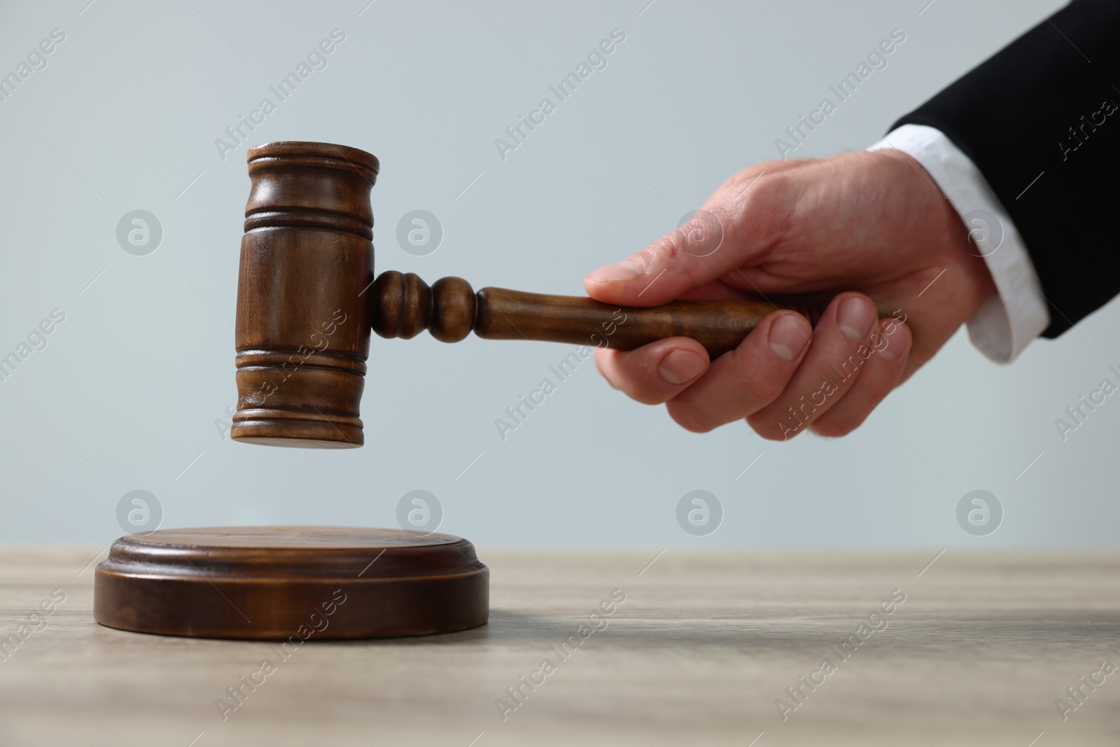 Photo of Judge with gavel sitting at wooden table against light grey background, closeup