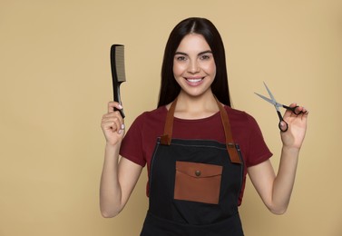 Portrait of happy hairdresser with professional scissors and comb on beige background