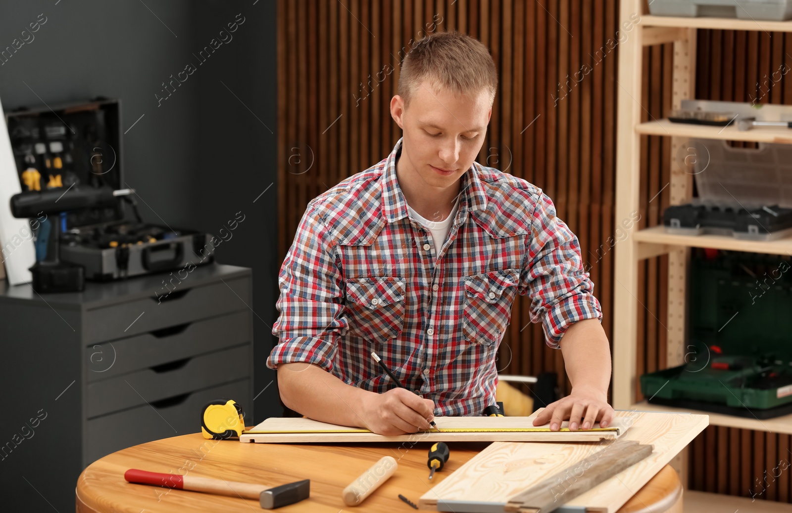 Photo of Handsome young working man making marks on timber at table indoors. Home repair