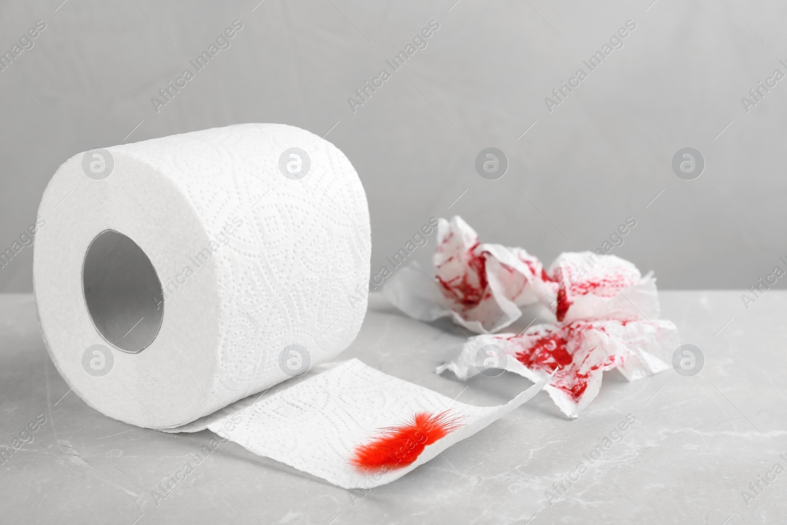 Photo of Roll of toilet paper and red feather on table. Hemorrhoid problems