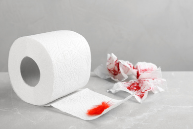 Roll of toilet paper and red feather on table. Hemorrhoid problems