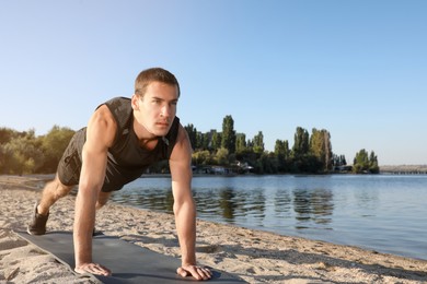 Photo of Sporty man doing straight arm plank exercise on beach
