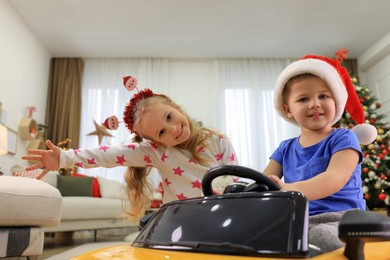 Cute little children playing with toy car in room decorated for Christmas