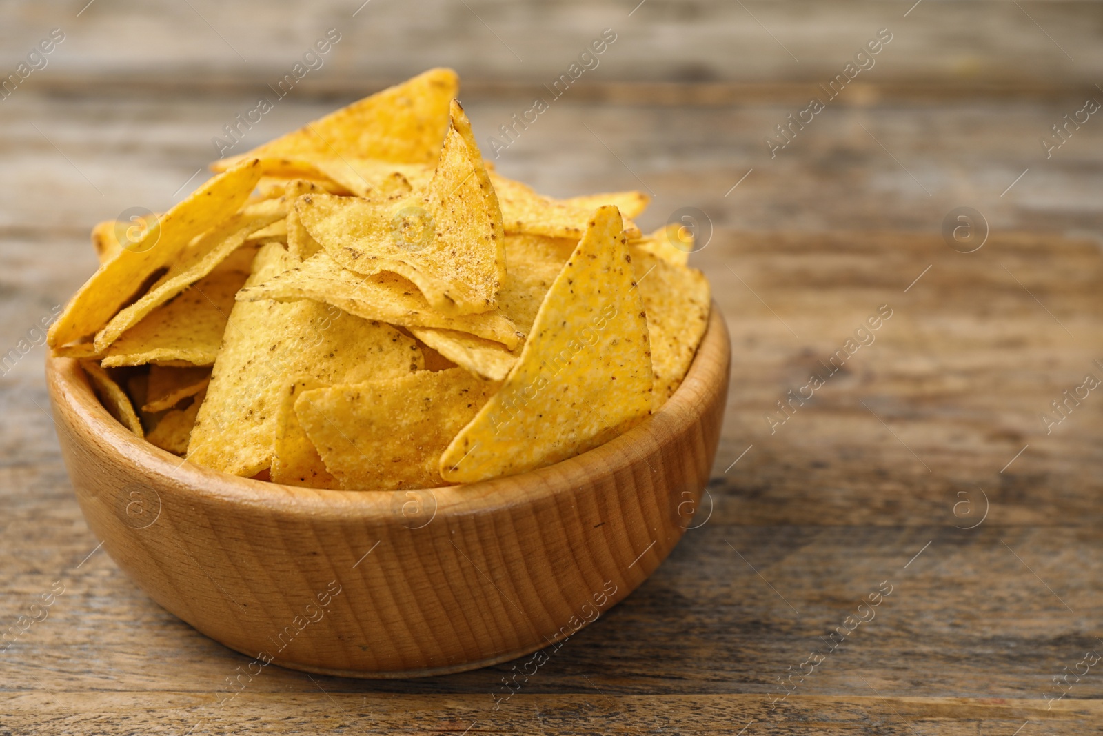 Photo of Bowl with tasty Mexican nachos chips on wooden table, space for text
