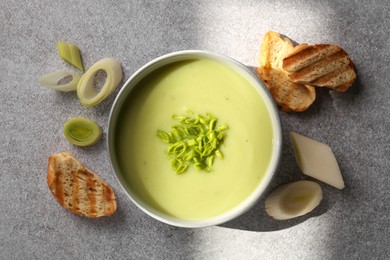 Bowl of delicious soup, cut leek and croutons on grey table, flat lay