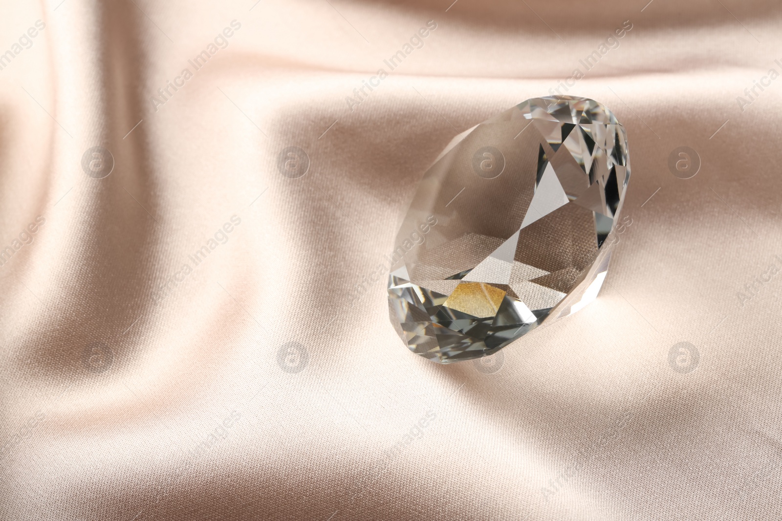 Photo of Beautiful shiny diamond on beige silky fabric, closeup. Space for text