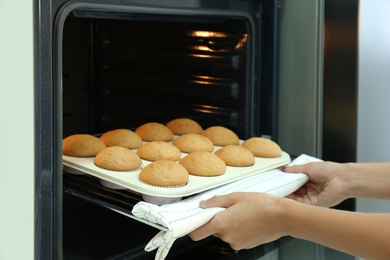 Photo of Woman taking cupcakes out of oven indoors, closeup