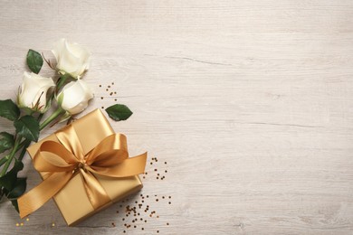Photo of Golden gift box and beautiful roses on wooden background, flat lay. Space for text