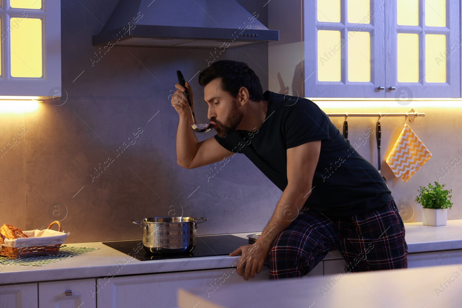 Photo of Man eating soup in kitchen at night. Bad habit