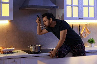 Photo of Man eating soup in kitchen at night. Bad habit