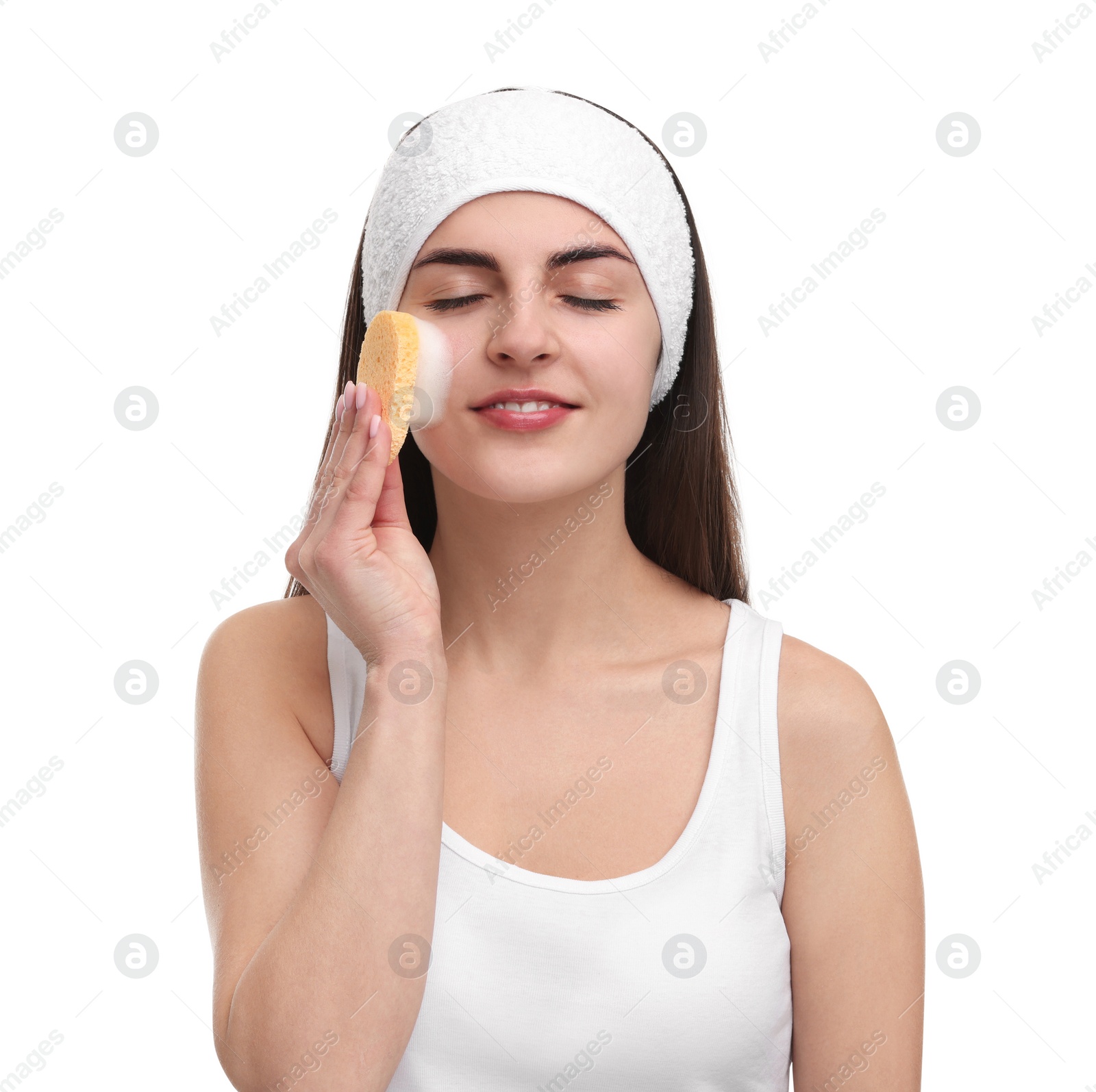 Photo of Young woman with headband washing her face using sponge on white background