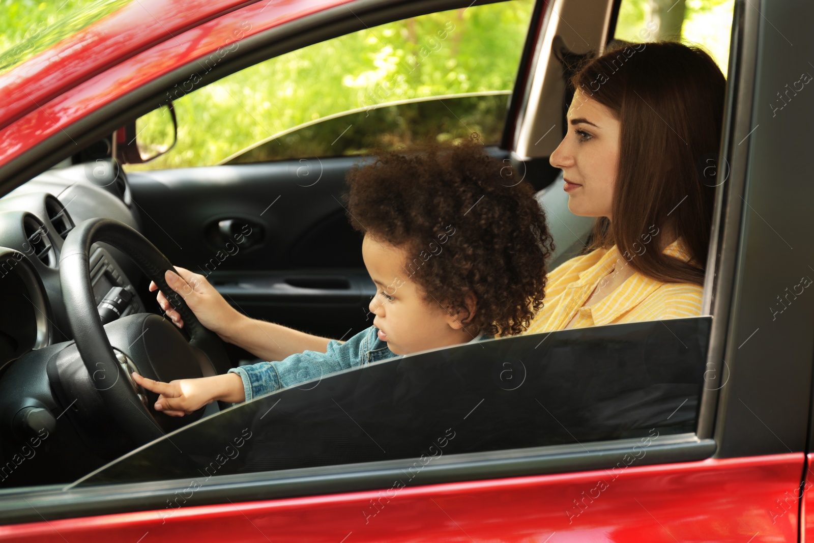 Photo of Mother with cute little daughter driving car together. Child in danger