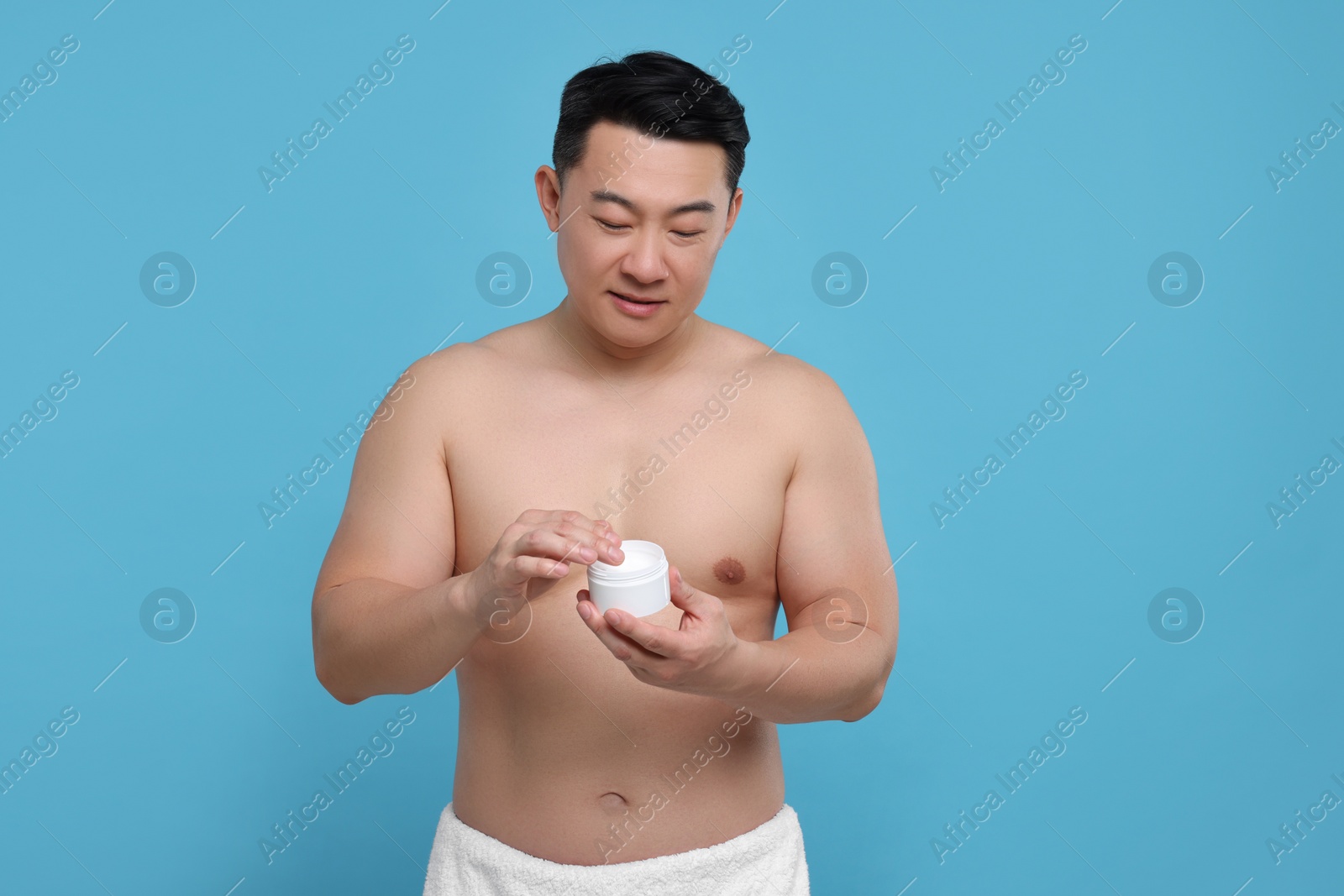 Photo of Handsome man with jar of body cream on light blue background