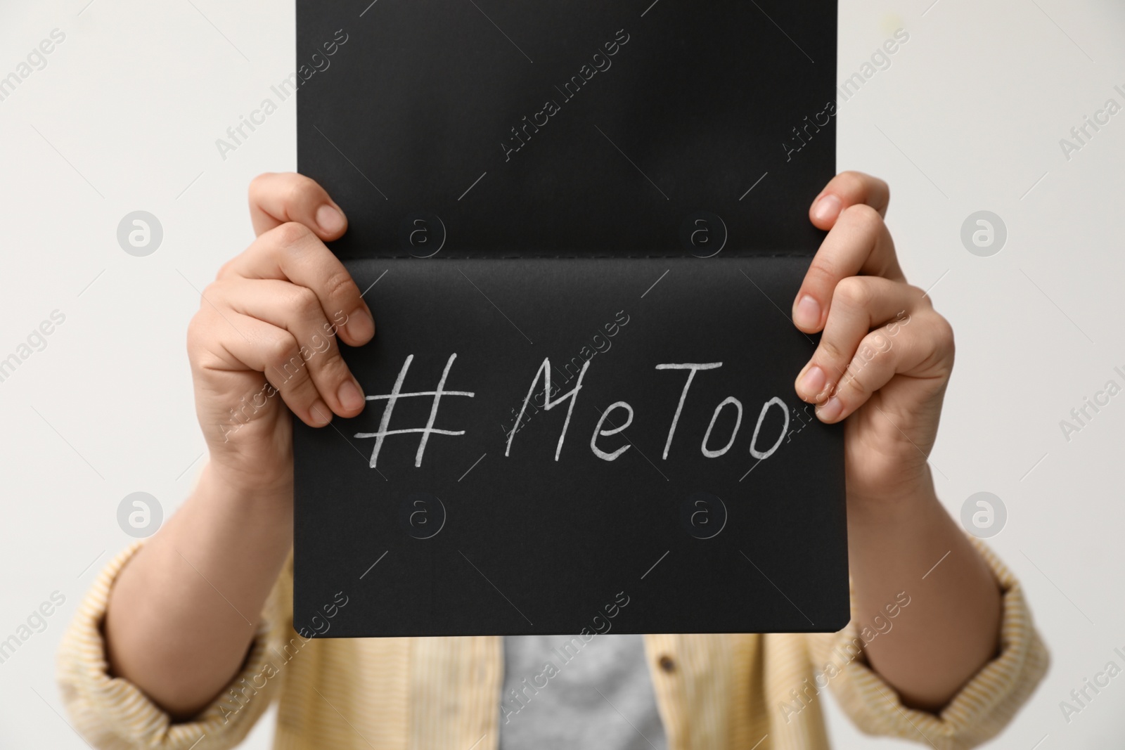 Photo of Woman holding notebook with hashtag MeToo against light background, closeup. Stop sexual assault