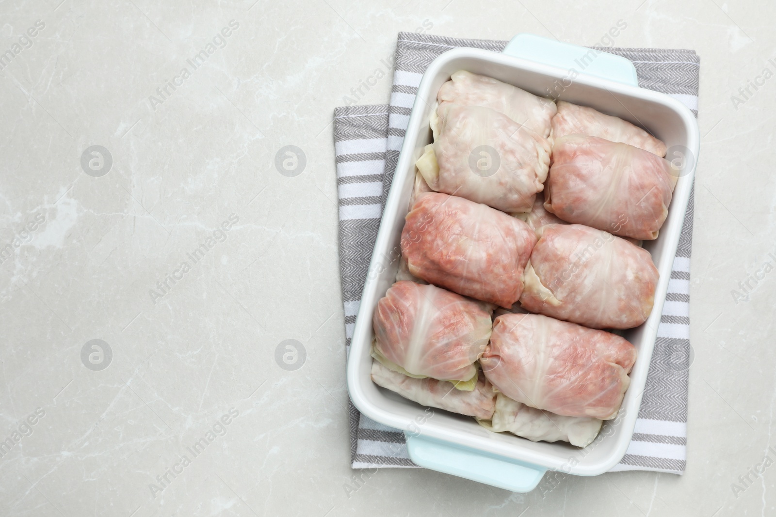 Photo of Uncooked stuffed cabbage rolls in baking dish on light grey table, top view. Space for text