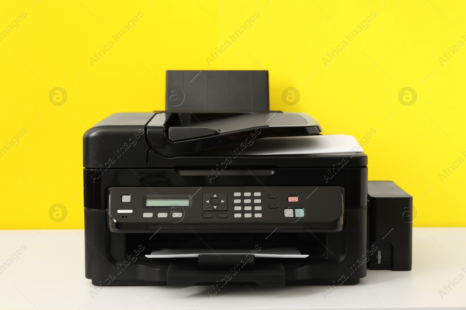 Photo of New modern printer on white table against yellow background