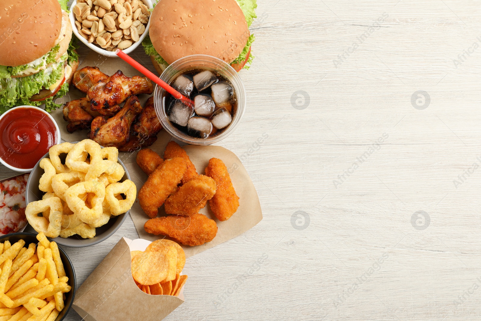 Photo of French fries, burgers and other fast food on white wooden table, flat lay with space for text