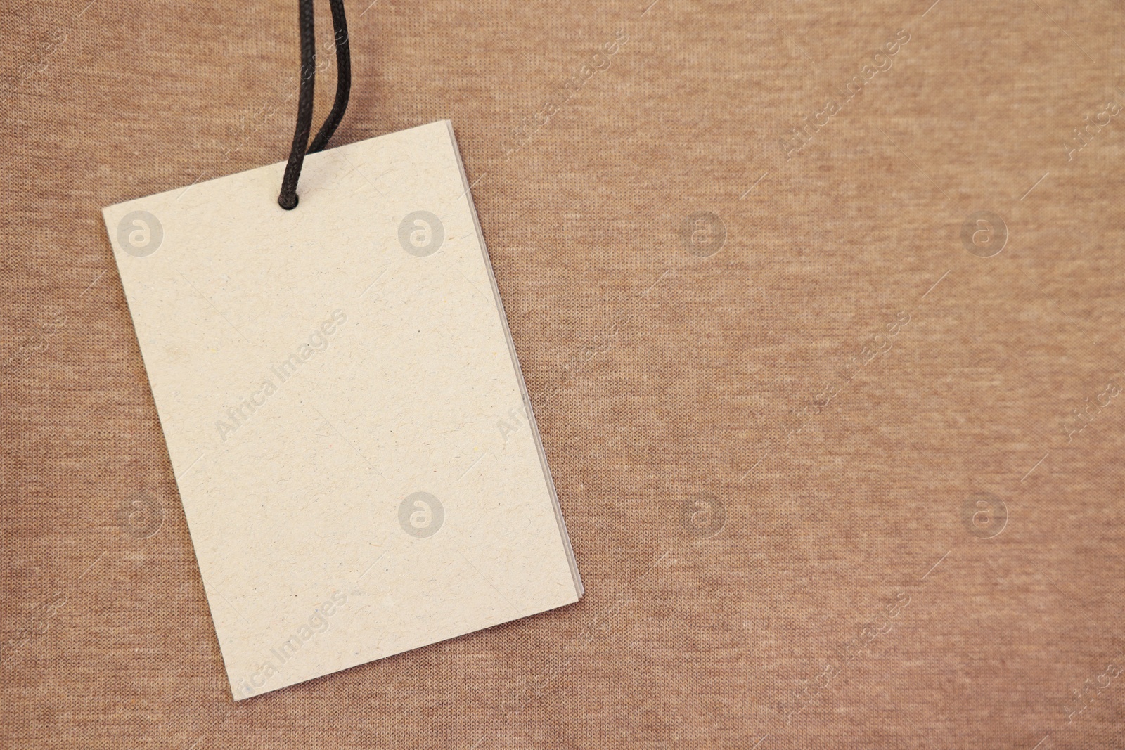 Photo of Cardboard tag on brown garment, top view. Space for text