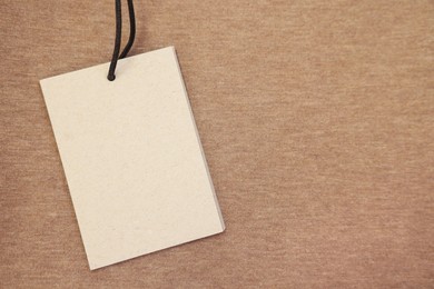 Photo of Cardboard tag on brown garment, top view. Space for text