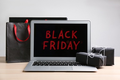 Photo of Laptop with Black Friday announcement, shopping bags and gifts on wooden table against white background