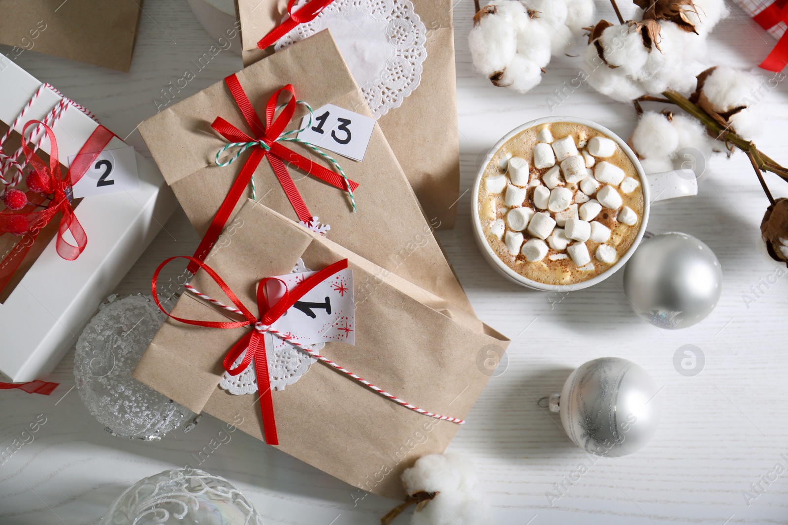 Photo of Flat lay composition with Christmas gifts, cup of marshmallow cocoa and festive decor on white wooden table. Creating Advent calendar