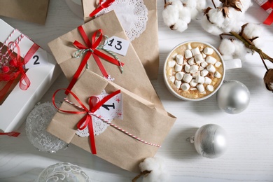 Flat lay composition with Christmas gifts, cup of marshmallow cocoa and festive decor on white wooden table. Creating Advent calendar