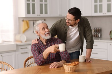 Photo of Happy son and his dad at wooden table in kitchen
