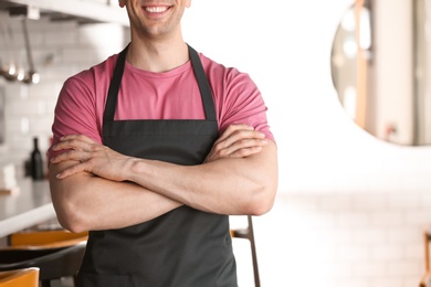 Photo of Young waiter in uniform at cafe