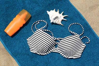 Photo of Blue beach towel, sunscreen, seashell and swimsuit on sand, flat lay
