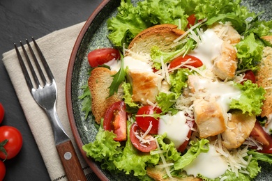 Photo of Delicious fresh Caesar salad on black table, closeup