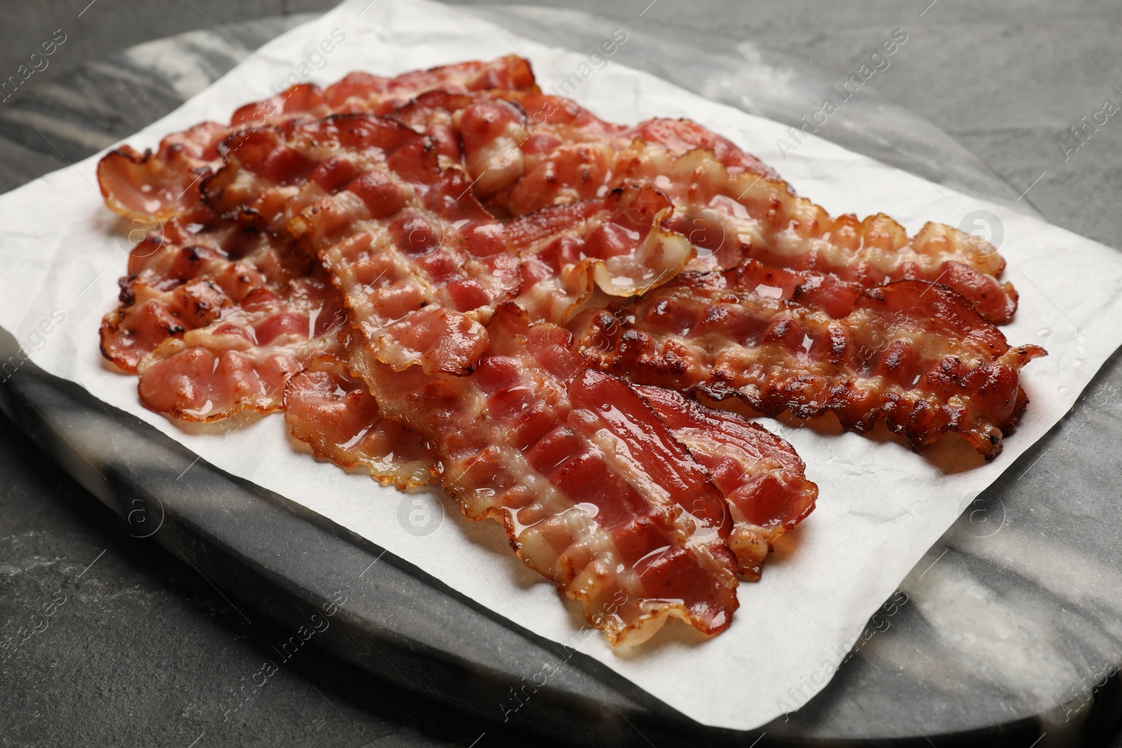 Photo of Fried bacon slices on dark table, closeup