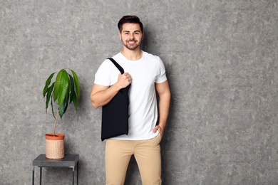 Photo of Portrait of young man with eco bag at table near grey wall. Space for text