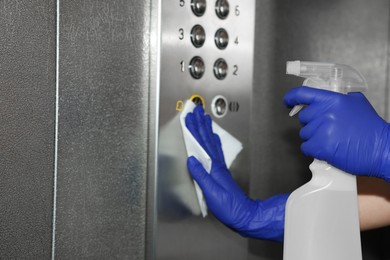 Photo of Woman wiping buttons of elevator`s panel with detergent and paper napkin, closeup