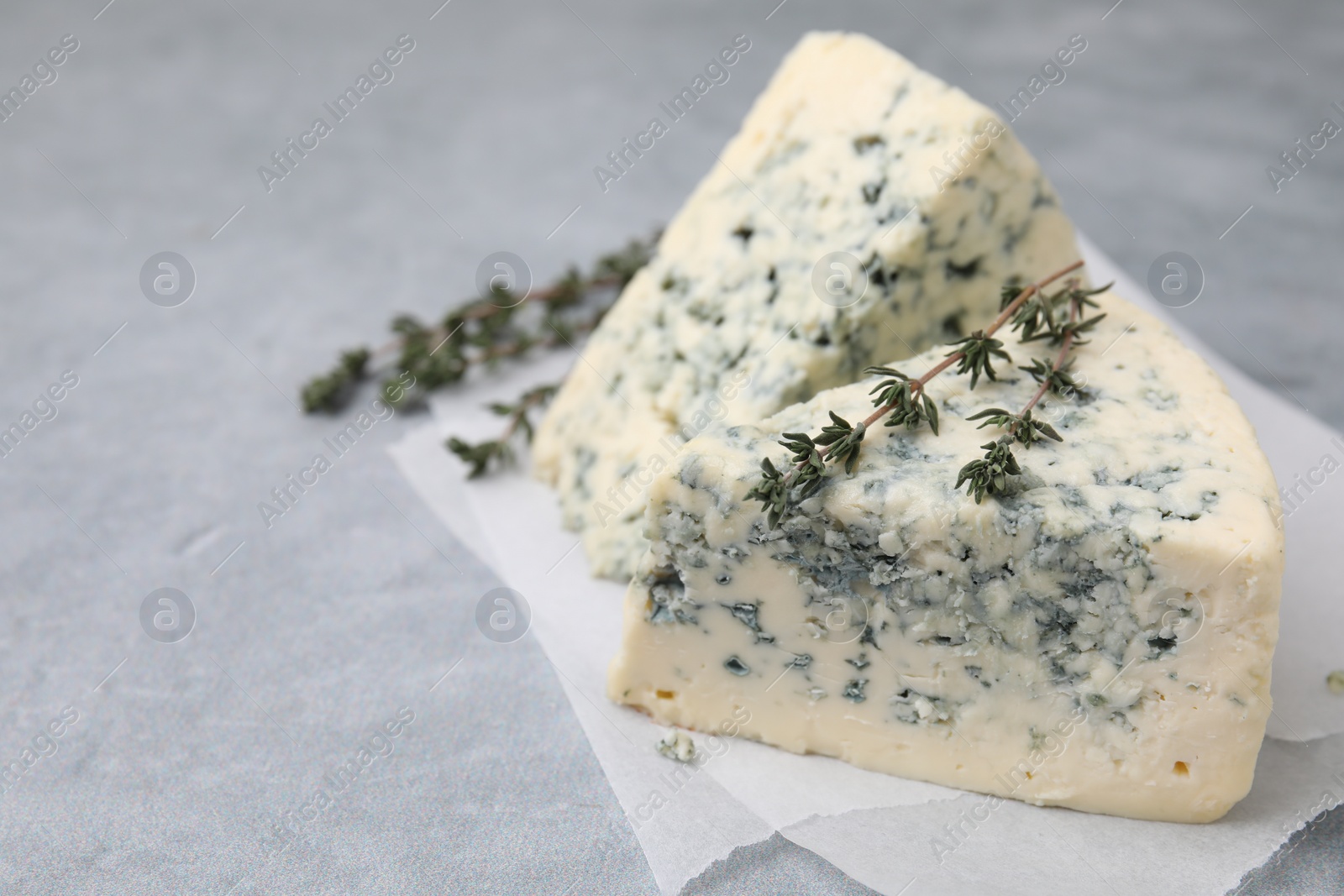 Photo of Tasty blue cheese with thyme on grey table. Space for text